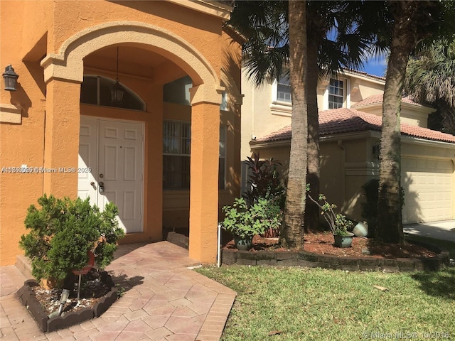 doorway to property featuring a garage, a tiled roof, and stucco siding