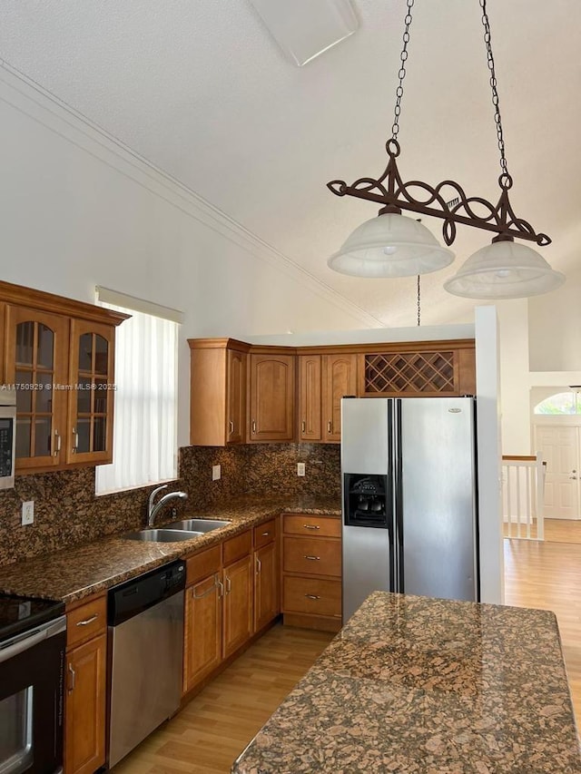 kitchen with a sink, vaulted ceiling, hanging light fixtures, appliances with stainless steel finishes, and brown cabinetry