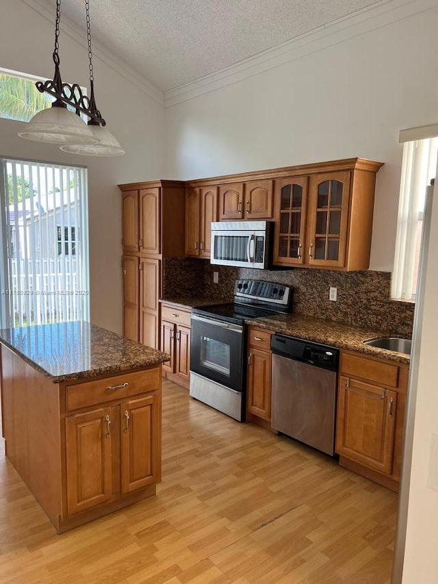 kitchen featuring pendant lighting, stainless steel appliances, glass insert cabinets, and brown cabinets