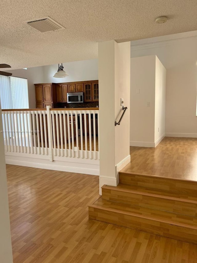 spare room featuring light wood-style floors, visible vents, a textured ceiling, and baseboards