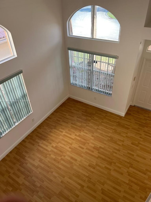 unfurnished room with a high ceiling, light wood-style flooring, and baseboards