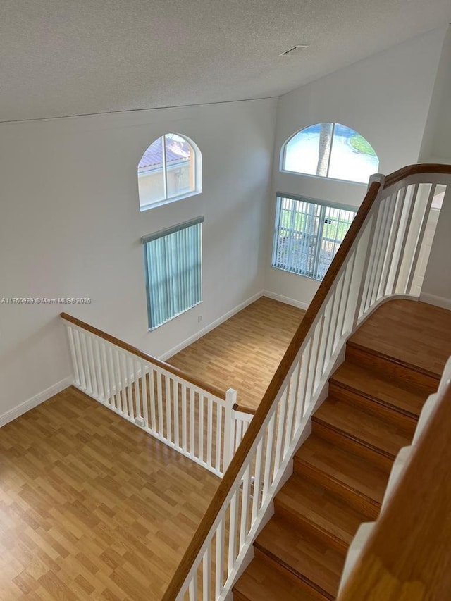 stairway with a textured ceiling, baseboards, and wood finished floors