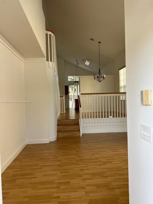 spare room featuring a chandelier, wood finished floors, baseboards, vaulted ceiling, and stairway