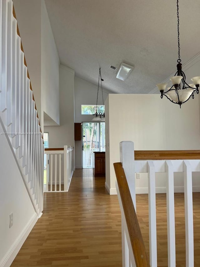 hallway featuring an inviting chandelier, baseboards, visible vents, and wood finished floors