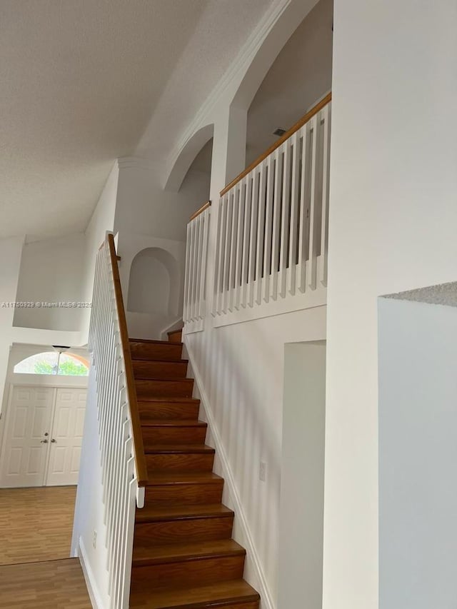 stairs with a textured ceiling, wood finished floors, a towering ceiling, and baseboards