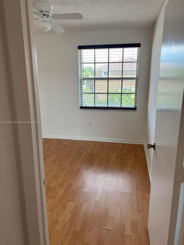 empty room with a textured ceiling, ceiling fan, light wood finished floors, and baseboards