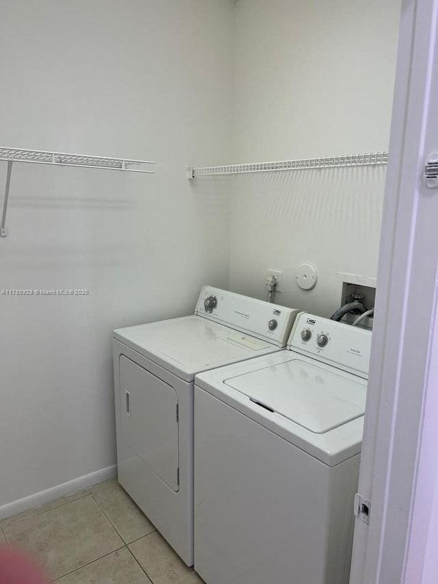 clothes washing area with light tile patterned floors, laundry area, baseboards, and washer and dryer