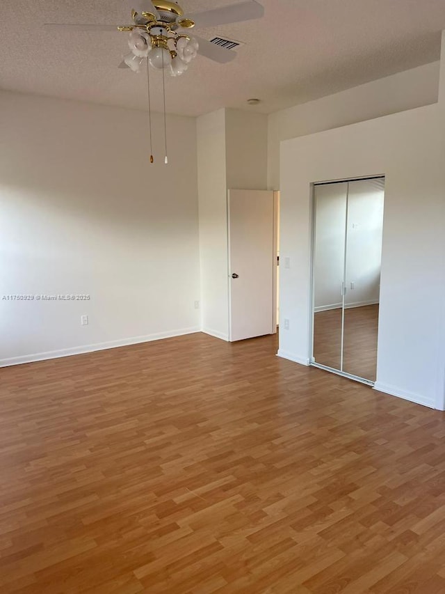 spare room with ceiling fan, a textured ceiling, wood finished floors, visible vents, and baseboards