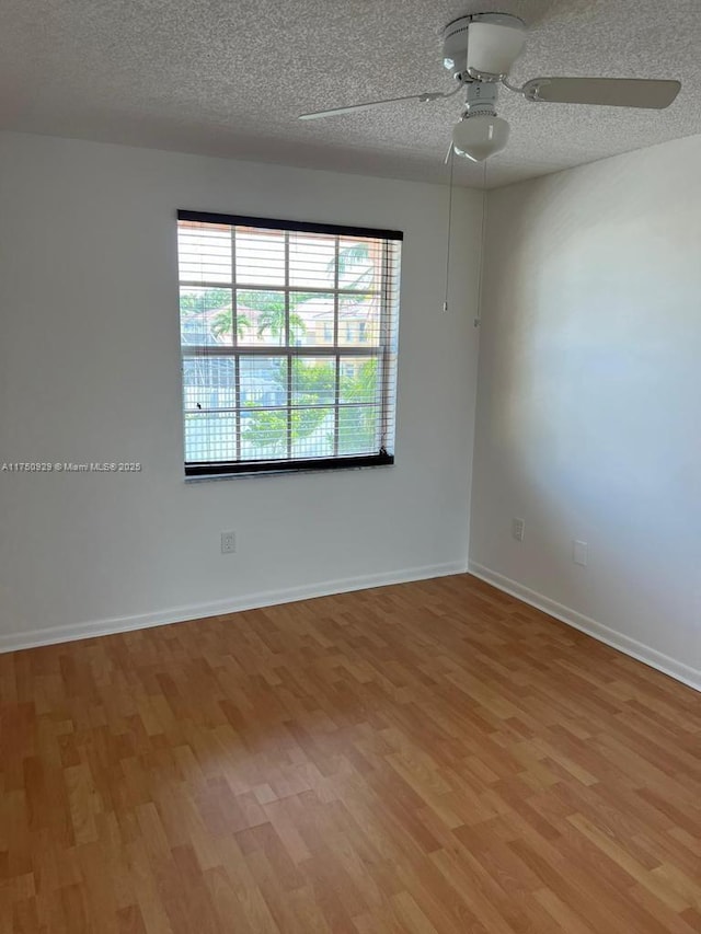 empty room with a textured ceiling, wood finished floors, a ceiling fan, and baseboards