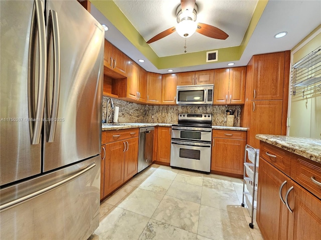 kitchen featuring stainless steel appliances, a sink, visible vents, backsplash, and light stone countertops