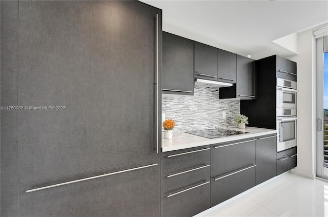 kitchen with gray cabinets, light countertops, decorative backsplash, under cabinet range hood, and black electric cooktop