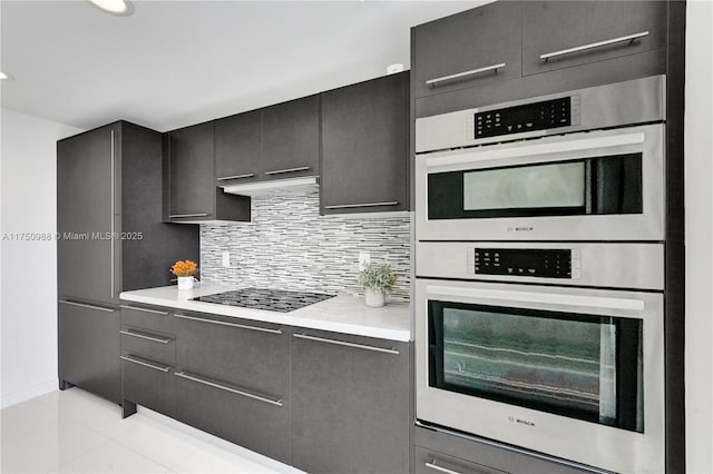 kitchen featuring black electric stovetop, light tile patterned floors, tasteful backsplash, light countertops, and double oven