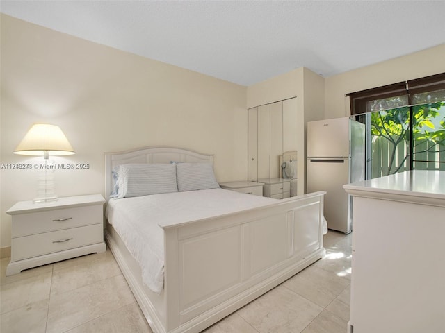 bedroom featuring light tile patterned floors, a closet, and freestanding refrigerator