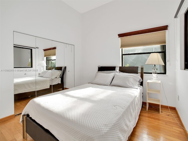 bedroom with a high ceiling, baseboards, and light wood finished floors