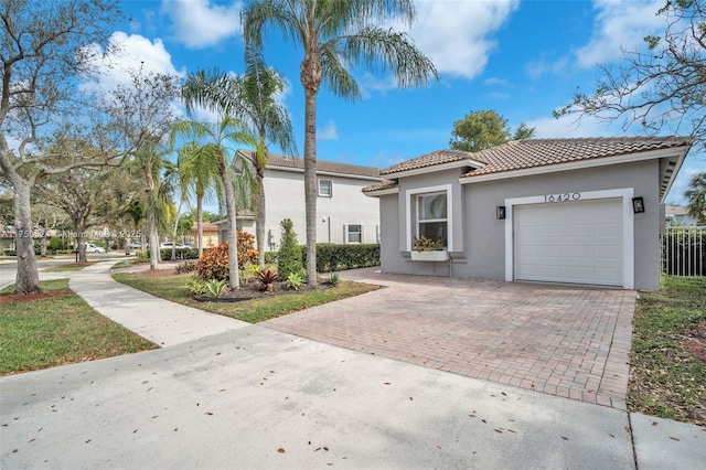 mediterranean / spanish-style home with an attached garage, a tiled roof, decorative driveway, and stucco siding