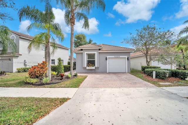 mediterranean / spanish-style house with decorative driveway, an attached garage, a tile roof, and stucco siding