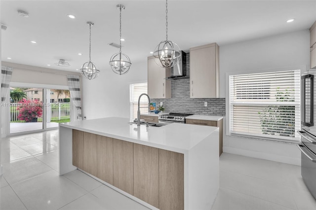 kitchen featuring wall chimney range hood, a kitchen island with sink, light countertops, and a wealth of natural light