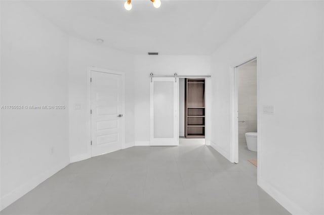 unfurnished bedroom featuring light tile patterned floors, a barn door, visible vents, baseboards, and ensuite bath