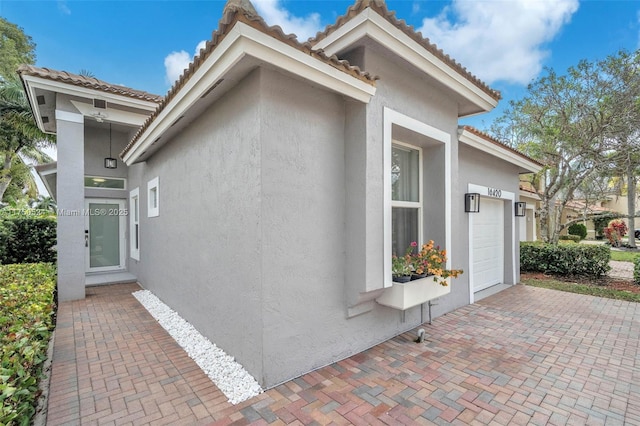 view of side of home featuring an attached garage, a tiled roof, decorative driveway, and stucco siding