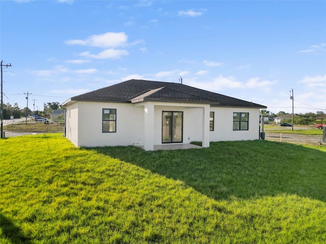 back of property with stucco siding, roof with shingles, and a yard