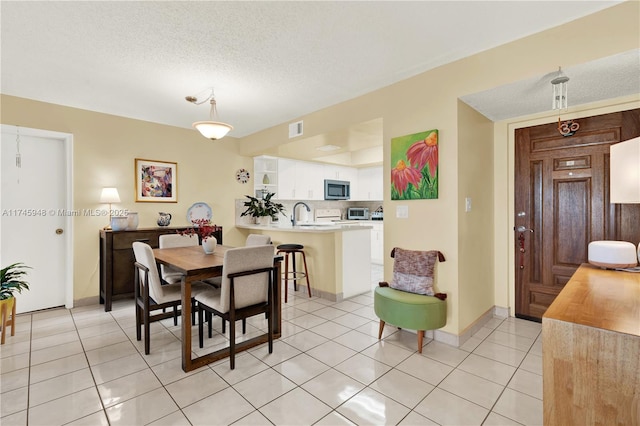 dining area featuring light tile patterned floors, baseboards, visible vents, and a textured ceiling