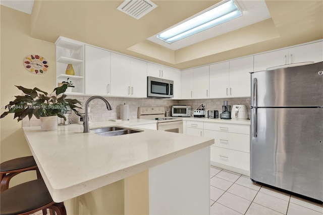 kitchen featuring a tray ceiling, open shelves, stainless steel appliances, a sink, and a peninsula