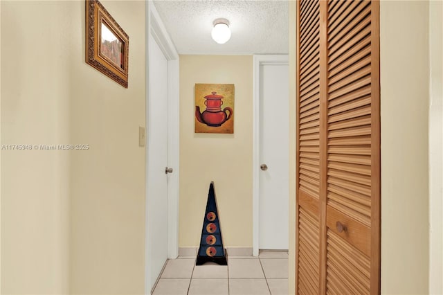 hall with baseboards, a textured ceiling, and light tile patterned flooring