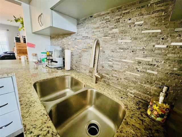 kitchen with decorative backsplash, light stone counters, white cabinets, and a sink