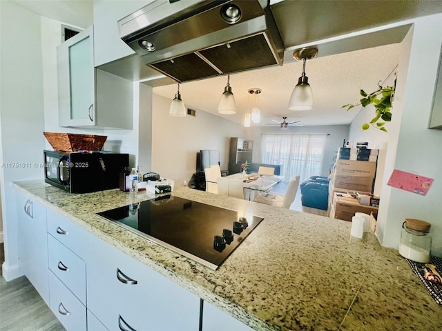 kitchen featuring light stone counters, hanging light fixtures, a ceiling fan, black appliances, and exhaust hood