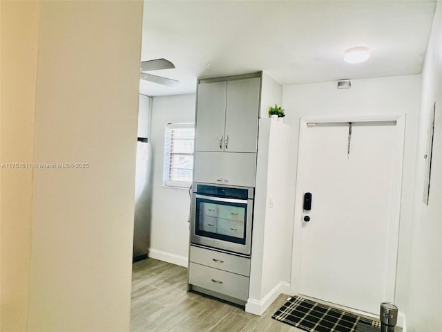 kitchen with stainless steel oven, baseboards, fridge, gray cabinets, and light wood finished floors