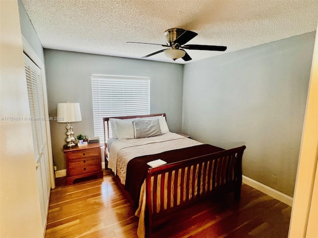 bedroom with a closet, ceiling fan, a textured ceiling, wood finished floors, and baseboards