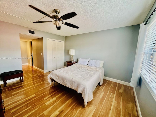 bedroom featuring visible vents, a textured ceiling, baseboards, and wood finished floors