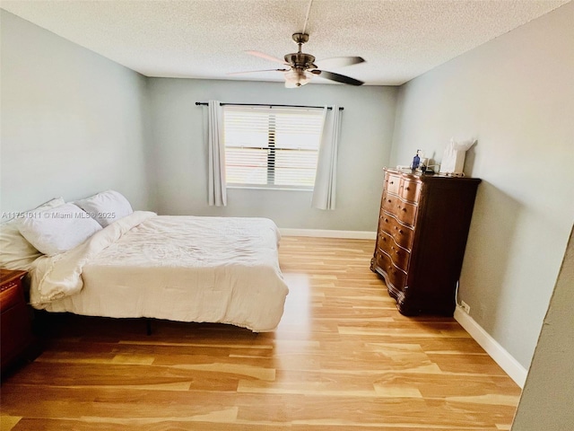 bedroom featuring light wood-style floors, a textured ceiling, baseboards, and a ceiling fan