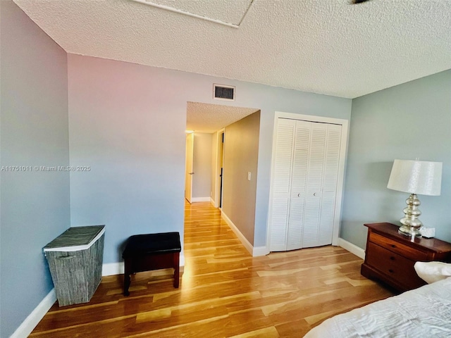 bedroom with baseboards, visible vents, wood finished floors, a textured ceiling, and a closet