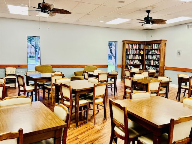 dining area featuring ceiling fan, a drop ceiling, visible vents, baseboards, and light wood finished floors