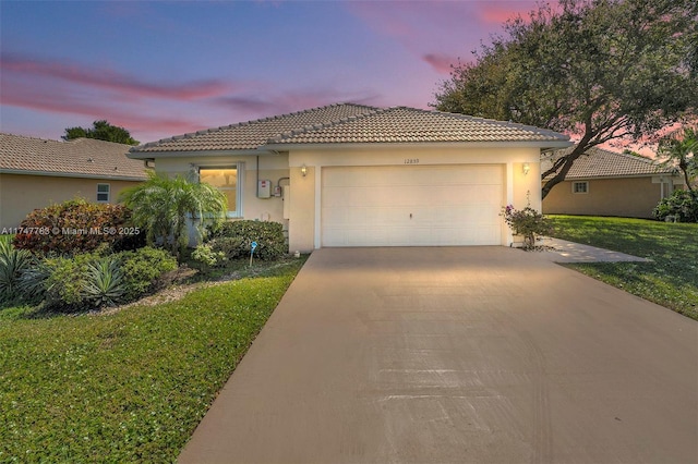 view of front of home featuring stucco siding, a lawn, driveway, a tile roof, and a garage