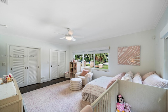 bedroom with multiple closets, ornamental molding, wood finished floors, and visible vents