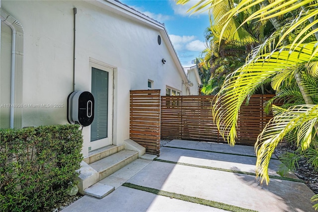 view of exterior entry with stucco siding and fence