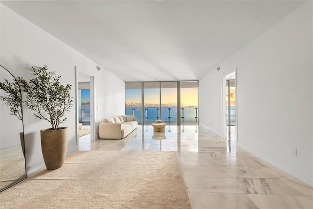 unfurnished living room featuring floor to ceiling windows, a water view, and baseboards