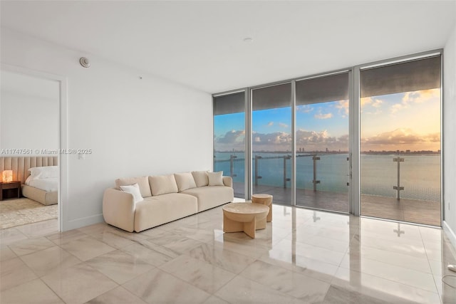 unfurnished living room featuring a water view, marble finish floor, baseboards, and floor to ceiling windows