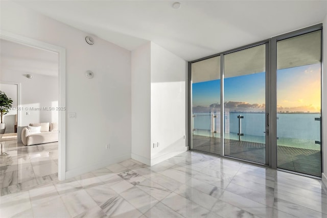 spare room featuring a wall of windows, a water view, and baseboards