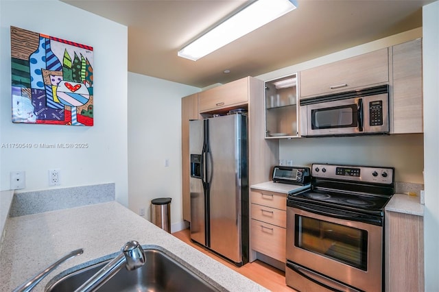 kitchen featuring light countertops, appliances with stainless steel finishes, a sink, and light brown cabinetry