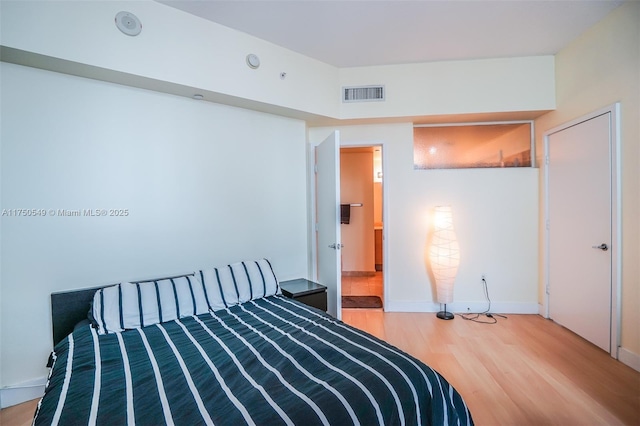 bedroom with baseboards, visible vents, and wood finished floors