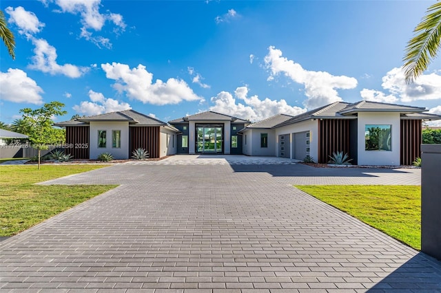 prairie-style house featuring stucco siding, a front lawn, decorative driveway, and a garage