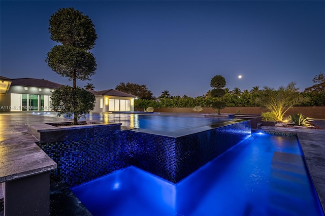 pool at night featuring an outdoor pool and fence