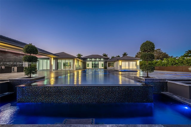 pool at dusk with an infinity pool, an outdoor structure, and fence