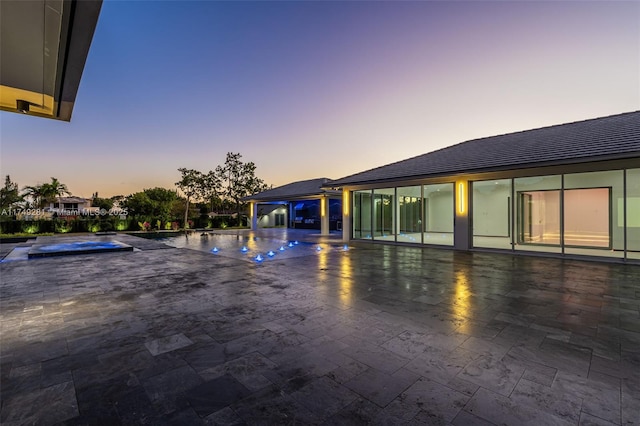 pool at dusk featuring an outdoor pool, a patio, and an in ground hot tub