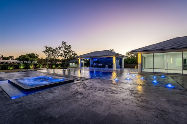 pool at dusk with fence, an in ground hot tub, an outdoor pool, a gazebo, and a patio area