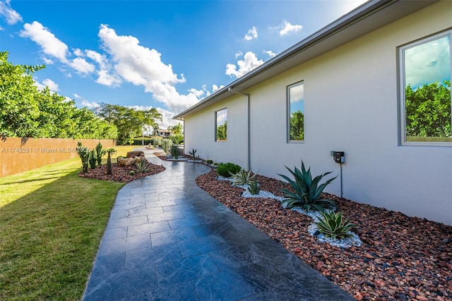 view of property exterior featuring stucco siding, a patio, a yard, and fence