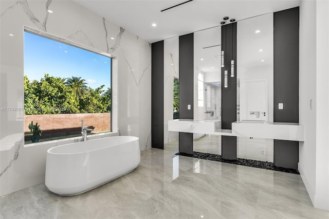 bathroom featuring marble finish floor, recessed lighting, a freestanding bath, stone wall, and vanity